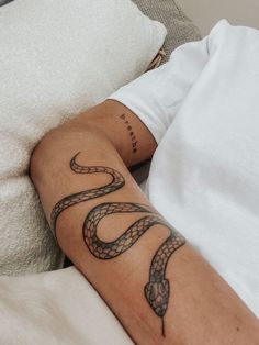 a man laying in bed with a tattoo on his arm and the word snake tattooed on his arm