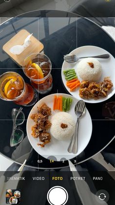 two plates with different foods on them sitting on a glass table next to glasses and utensils