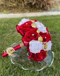 a red and white bridal bouquet sitting on top of a glass plate in the grass