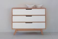 two white bowls sit on top of a wooden dresser next to a wall and floor