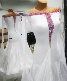 two white dresses with colorful sequins on them are displayed in a shop window