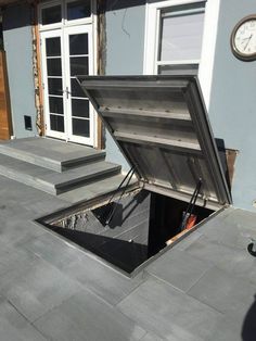 an open trunk sitting on top of a patio next to a clock and steps in front of a house