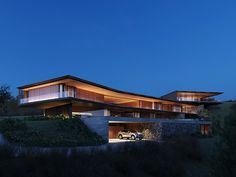 a car is parked in front of a modern house at night with its lights on