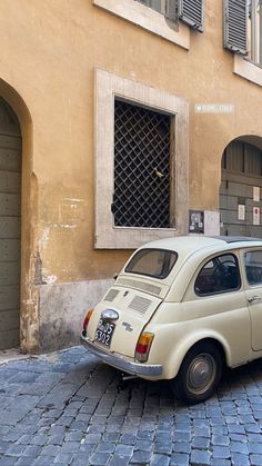 an old white car parked on the side of a street in front of a building