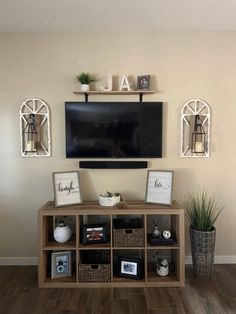 a flat screen tv mounted on the wall above a wooden shelf with baskets and plants