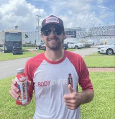 a man holding two cans of energy drink and giving the thumbs up in front of him