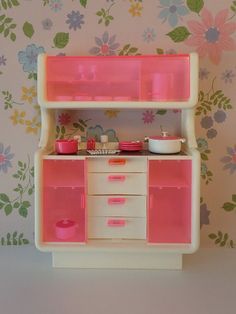 a doll house kitchen with pink and white cabinets, flowers on the wall behind it