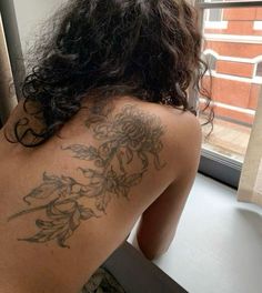 a woman with a tattoo on her back looking out the window