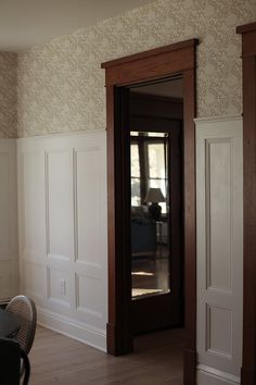 an empty room with wooden floors and white paneling on the walls, along with a black chair