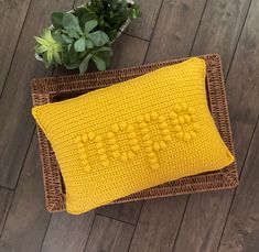 a yellow knitted pillow sitting on top of a wooden floor next to a potted plant