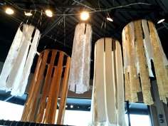 some lights are hanging from the ceiling in a room with wooden poles and cloths