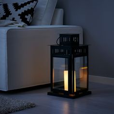 a black lantern sitting on top of a hard wood floor next to a white couch