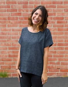 a woman standing in front of a brick wall wearing black pants and a gray top