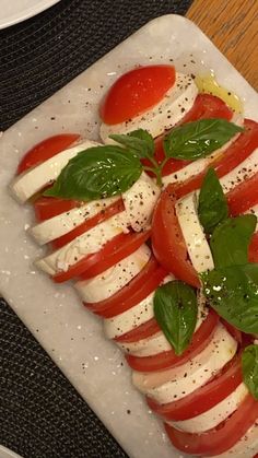 tomatoes, mozzarella and basil are arranged on a white platter with silverware