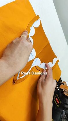 someone is cutting out paper with scissors on a piece of yellow material that has been cut in half