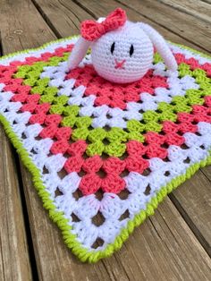 a crocheted blanket with a stuffed animal in the middle on a wooden surface