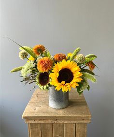 an arrangement of sunflowers and other flowers in a vase on a wooden table