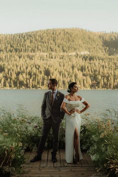 a bride and groom standing on a dock by the water