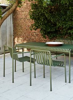 a green table and chairs sitting next to each other on a sidewalk near a brick wall