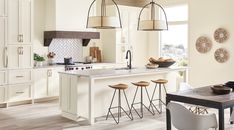 a kitchen with white cabinets and gold pendant lights hanging from the ceiling over the island