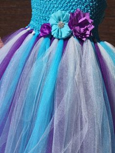 She will feel like a 👸 and look like royalty in this turquoise flower girl dress. This dress is perfect for your wedding! It is made with plum purple, turquoise, grey and silver glitter throughout making her shine and sparkle. The dress has an empire waist. There are 3 flowers in turquoise and purple for added cuteness. The turquoise top is lined for added softness and isn't see through. The satin straps cross cross and tie in the back which can be loosened or tighten for a secure fit. When mea Turquoise Combinations, Turquoise Flower Girl Dress, Blue Tutu Dress, Purple Wedding Inspiration, Fall Beach, Blue Tutu, Tulle Flower Girl Dress