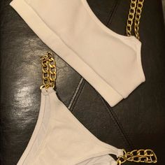 two pieces of white clothing with gold chains attached to the top and bottom, sitting on a black leather surface