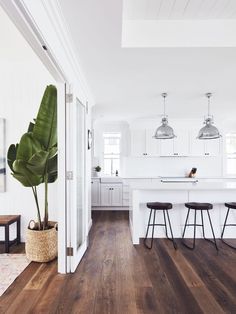 a kitchen with white walls and wooden floors, two stools in front of the counter