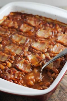 a white dish filled with baked beans and meat in gravy on top of a wooden table