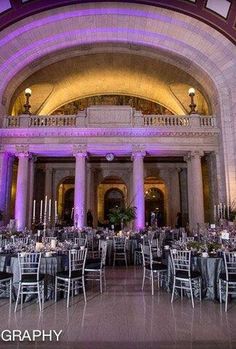 the inside of a large building with tables and chairs set up for an event in front of purple lighting