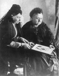 an old photo of two women sitting down and looking at something on the table in front of them