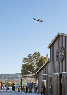 an airplane flying over a group of people standing outside of a building with a clock on it's side