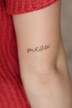 a woman's arm with the word meow written in cursive font