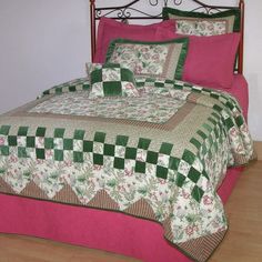 a bed with green and pink bedspread on top of wooden floor next to white wall