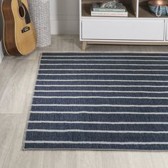 a blue and white striped rug on the floor next to a book shelf with a guitar