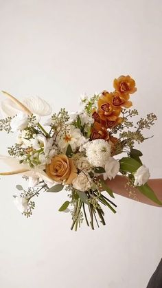 a woman holding a bouquet of flowers in her hand with white and orange flowers on it