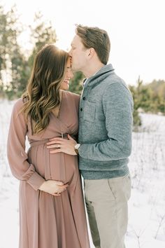 a pregnant couple standing in the snow together