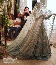 a woman in a wedding dress is taking a photo with her cell phone while people look on