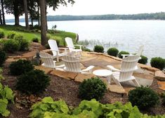 white lawn chairs sitting on top of a stone walkway next to a body of water