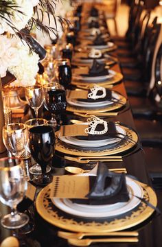 a long table is set with black and gold place settings for formal dinnereons