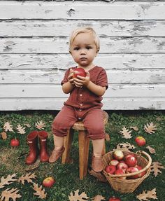 a little boy sitting on top of a wooden chair with apples in front of him