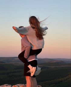 two people standing on top of a mountain with their arms around each other and one person holding the other