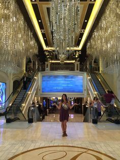 a woman standing in the middle of a lobby with chandeliers hanging from the ceiling