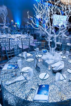 the table is set for an event with silver linens and white tree centerpieces