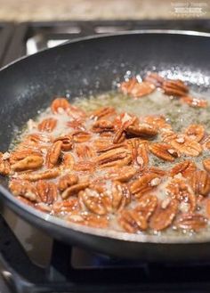 a frying pan filled with cooked pecans on top of an electric burner