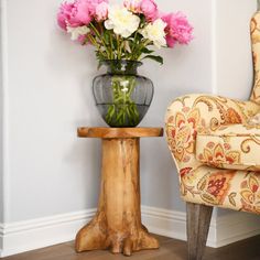 a chair next to a vase with flowers in it and a table on the floor