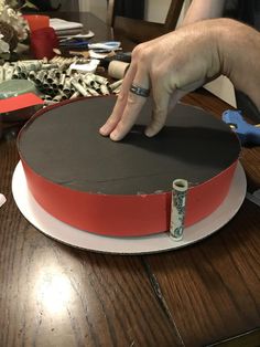 a hand is pointing at the top of a round cake with red and white trim