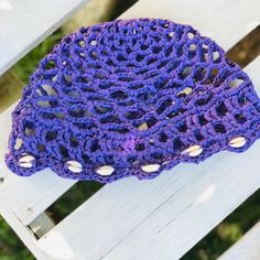 a purple crocheted hat sitting on top of a wooden bench