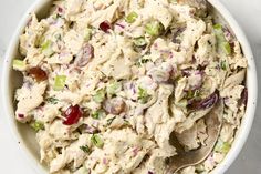 a white bowl filled with chicken salad on top of a table next to a spoon