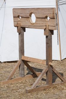 a wooden chair sitting on top of dry grass next to a white tent with a chain hanging from it's side