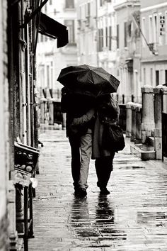 black and white photograph of two people walking down the street in the rain holding umbrellas